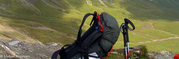 Gefüller Wanderrucksack und Wanderstöcke vor grünem Hochgebirge